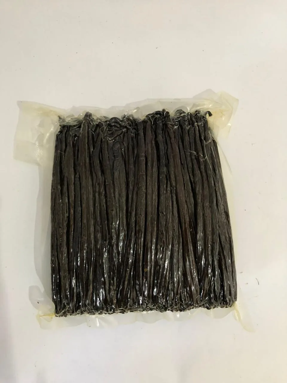 Vacuum-sealed bag of cured vanilla beans, flat on a white surface